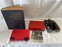 Overview of lot showing auto repair manual, Snap-on red tool case, red metal toolbox, wire brushes, and instruction manual.