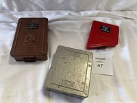 Three metal tool boxes set on white cloth: brown Lawson Products, silver Dormer Sheffield England, red Snap On.