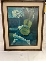 Full front view of framed art print of The Old Guitarist by Picasso with brown wood frame and light fabric mat.