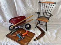 Photo showing the red Radio Flyer wagon with wooden handles, small black spindle back chair, Magic 8 Ball, wooden board with two figurines, and curved wooden decorative piece.