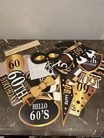 Assorted 60th birthday decorations including signs, masks, bow ties, and hats spread on a dark marble surface.