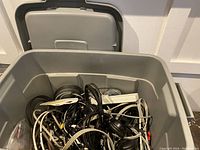 Photo showing open gray plastic bin filled with assorted electric cables and power strips, tangled inside.