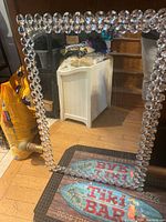 Mirror leaning against furniture showing crystal bead frame and reflective surface with slight smudges and dust.