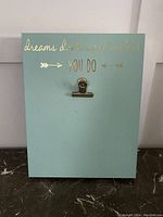 Front view of light blue clipboard with gold text and metal clip