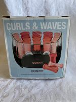 Photo of the Conair hot curlers box showing the set of red plastic thermal rollers arranged in the black base unit with a transparent cover.