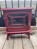 Front view of the red electric fireplace stove showing the glass door and legs.