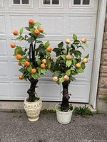 Photo showing two faux trees, one orange tree and one peach tree, both in pots against a garage door background