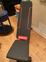 Front view of black MagicFit workout bench showing padded backrest with red trim and MagicFit logo.