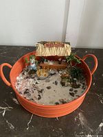 Photo showing entire mini tiki bar setup inside orange container with sand, shells, and figurines.