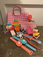 Photo of assorted pop it sensory toys and fidget toys including two pink Pop It bags, a cupcake-shaped toy, wristband fidgets, a Rubik's cube puzzle, and multiple small Pop It figures in various colors and shapes.
