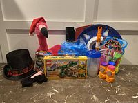 Lot of various toys including LEGO Creator 3in1 set, Catch N Cops toy package, bubble solution bottles, a pink flamingo plush, plaid top hat, blue ruffle accessory, two snowman plates, clear container, and bubble blower.