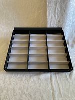 Black and white rectangular tray with 18 slots for storing eyeglasses or sunglasses.