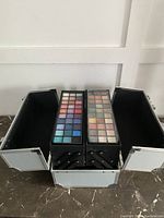 Open silver makeup case with two large eyeshadow palettes in two extended compartments showing variety of colors