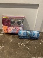 Overall view of the sunglasses in holographic bag and blue Cynthia Bailey glass case on the surface.