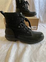 Side view of a new black UGG boot showing the lace-up front, textured and smooth material combination, and sole details.