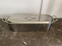 Closed stainless steel meatloaf pan viewed from the front with lid on, showing rectangular shape and side handles.