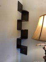 Photo of one dark wood corner shelf mounted on a wall showing five angular shelves with slight wear.