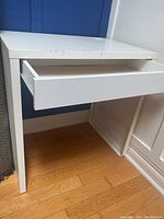 Close up of white IKEA desk showing pull-out drawer and signs of wear on surface and edge.