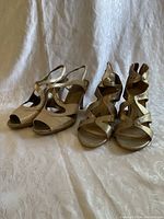 Two pairs of women's gold sparkle sandals displayed side-by-side on a white backdrop. One pair has wedge heels with cutout strappy design; the other is a heeled peep-toe sandal with ankle strap.