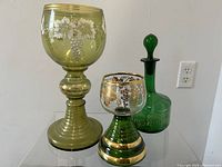 Photo showing three antique Bohemian glass vessels: tall yellow-green goblet, smaller green goblet, and green decanter with stopper.