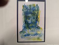 Close-up view of the framed watercolor painting depicting an abstract ethereal face in blue, green, and yellow hues.