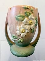 Front view of Roseville White Rose pottery vase with raised white flower decoration on pink and green background.