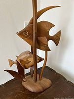Side view of the teak wood fish and reeds sculpture showing two carved fish and wooden reeds mounted on a smooth wooden base.