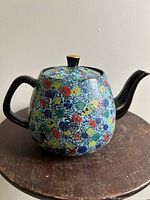 Front side view of ceramic teapot showing colorful splatter pattern and glossy finish
