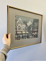 Framed Paris city view art print held against wall showing the front view and scale relative to hand.