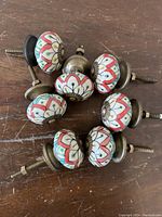 Seven vintage porcelain drawer knobs arranged in a circle on a wooden surface showing their colorful Moorish style patterns and brass fittings.