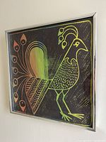 Framed 1970's peacock silkscreen linocut artwork showing a stylized bird in green, brown and orange on black background.