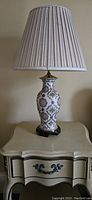 Single photo of one lamp showing ceramic floral design, wood base, 3-way switch, and pleated fabric shade.