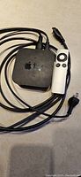 Apple TV device with remote control and attached cables on a surface.