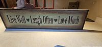 Wooden sign with inspirational text 'Live Well ♥ Laugh Often ♥ Love Much' on a framed rustic background.