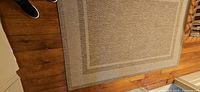 Photo showing rectangular brown and beige jute rug with a geometric patterned border and plain center area on wooden floor.