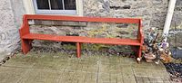 Red-orange wooden outdoor bench against stone wall, measuring approximately 95 inches long and 36 inches high.
