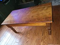 Photo of a rectangular wooden coffee table showing a medium brown finish, slight scratches on the tabletop, and turned legs on a hardwood floor.