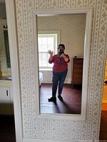 Full view of the mirror reflecting a person and part of a room showing the frame and the reflective surface.