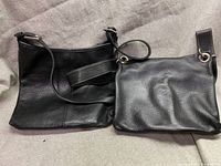Two black Roots leather shoulder bags laid on a fabric surface, showing front and back sides.