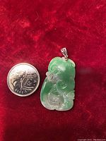 Jade pendant next to a quarter coin for size reference, showing green and translucent carved jade with a white gold clasp at the top.