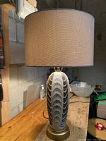Full view of the lamp showing the ribbed ceramic body with wave pattern, metal base, and beige fabric shade.