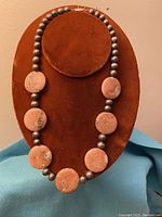 Full view of necklace displayed on a brown stand showing seven large flat oval-shaped pink potato pearl beads interspersed with smaller metallic silver round beads.
