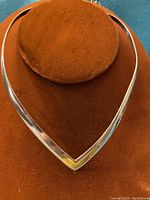 Front view of the polished sterling silver V shaped necklace choker displayed on an orange velvet stand.