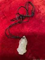 Front view of translucent carved stone pendant showing detailed figure and black braided necklace on a red background.