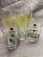 Set of 6 Bacardi glasses on fabric background including 2 short commemorative anniversary glasses and 4 taller Bacardi Limon Run glasses with gold bat logos