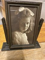Front view of vintage wooden swiveling picture frame holding black and white child's portrait photo.