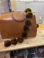 Vintage brown leather doctors medicine bag with rabbit fur scarf draped on and around it, showing front side and scarf detail.