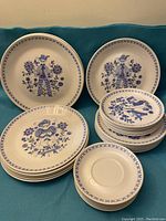 Overview of entire set including 2 large serving bowls, stacks of dinner plates, salad plates, bread & butter plates, saucers and soup bowls on teal background