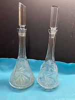 Two vintage leaded crystal glass decanters with pinwheel cut patterns and heavy faceted stoppers placed on a blue cloth against a black background.