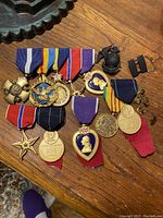 Top view of multiple vintage US military medals and insignia laid out on a table, showing ribbons and medal details